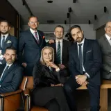 Grupa siedmiu profesjonalistów w garniturach, w tym jedna kobieta, pozuje do zdjęcia.