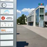 Tablica z nazwami firm, w tym "BiG Biuro Rachunkowe", przed nowoczesnym budynkiem biurowym.
