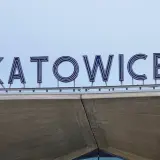 Napis "KATOWICE" z niebieskimi neonami na tle jasnego nieba, nad betonową konstrukcją.