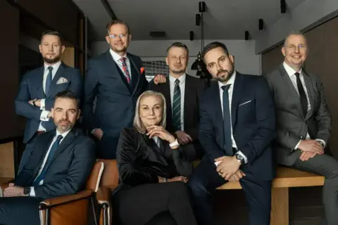 Grupa siedmiu profesjonalistów w garniturach, w tym jedna kobieta, pozuje do zdjęcia.