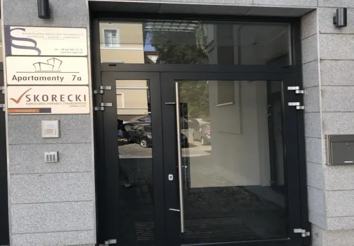 Wejście do budynku z tabliczkami: Kancelaria Radców Prawnych, Apartamenty 7a, Kancelaria Doradcy Finansowego SKORECKI.