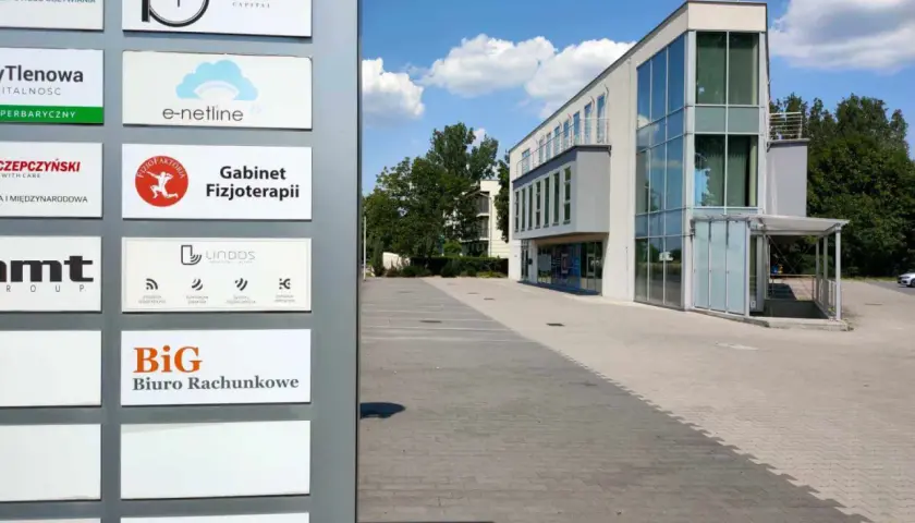 Tablica z nazwami firm, w tym "BiG Biuro Rachunkowe", przed nowoczesnym budynkiem biurowym.