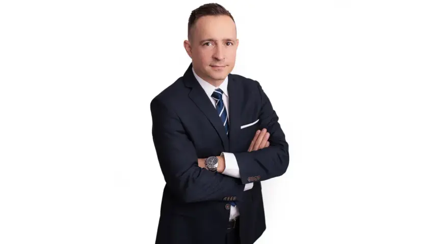 Mężczyzna w garniturze ze skrzyżowanymi rękami, na białym tle.