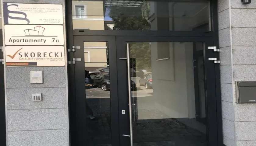 Wejście do budynku z tabliczkami: Kancelaria Radców Prawnych, Apartamenty 7a, Kancelaria Doradcy Finansowego SKORECKI.