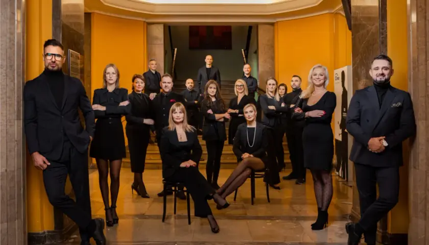 Grupa profesjonalistów w czarnych strojach pozuje w eleganckim wnętrzu.
