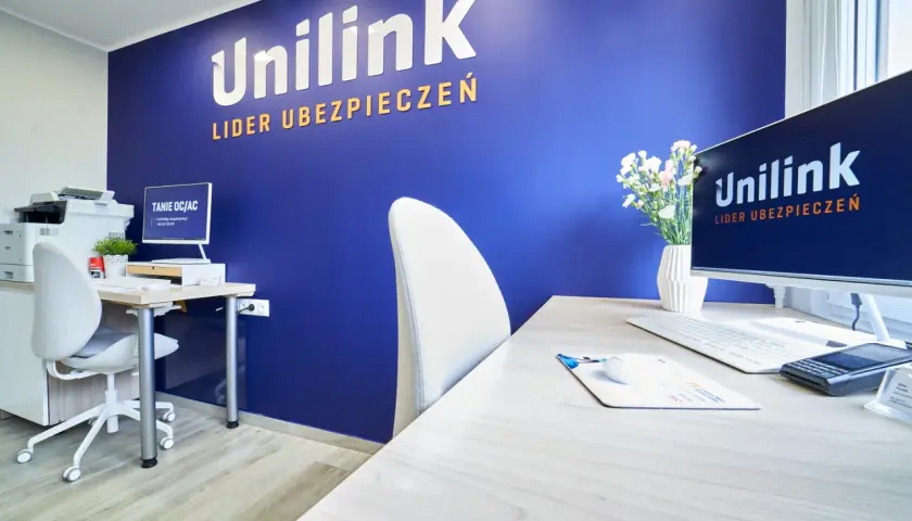 Biuro z niebieską ścianą z logo Unilink, biurkiem, komputerem i krzesłem.