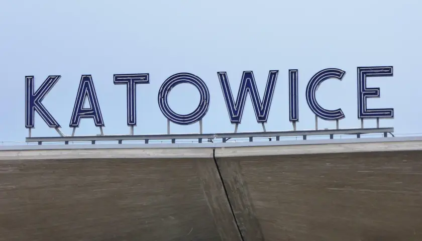 Napis "KATOWICE" z niebieskimi neonami na tle jasnego nieba, nad betonową konstrukcją.